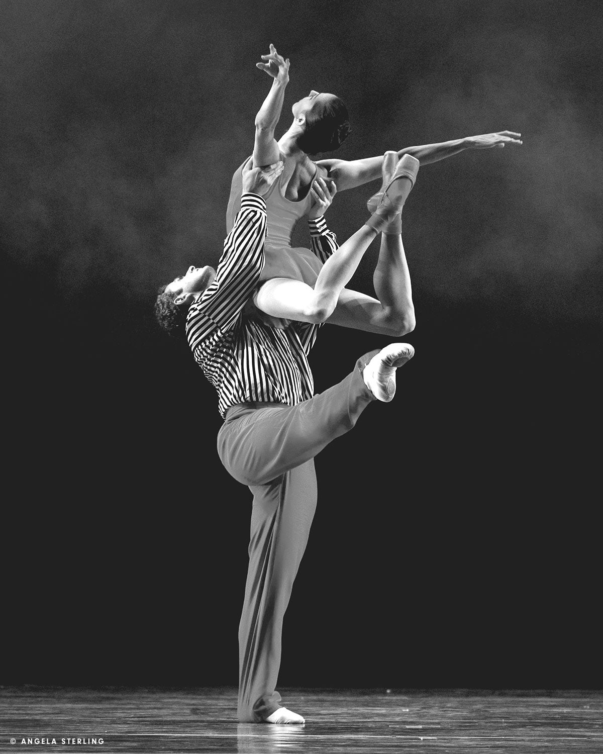 Jordan lifts a woman over head while standing on one leg in performance for Twyla Tharp's In The Upper Room. The dancers wear red solid and black and white striped designs by Norma Kamali.