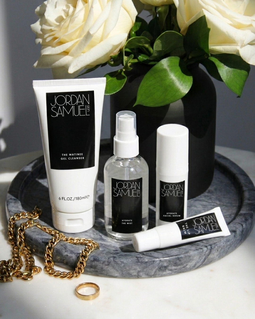 Jordan Samuel skincare products on a tray with flowers and jewelry