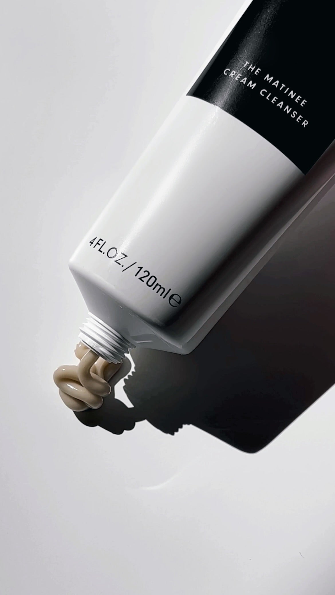 Tightly cropped image of khaki colored cleanser being squeezed from the white tube with black label of The Matinee Cream Cleanser.