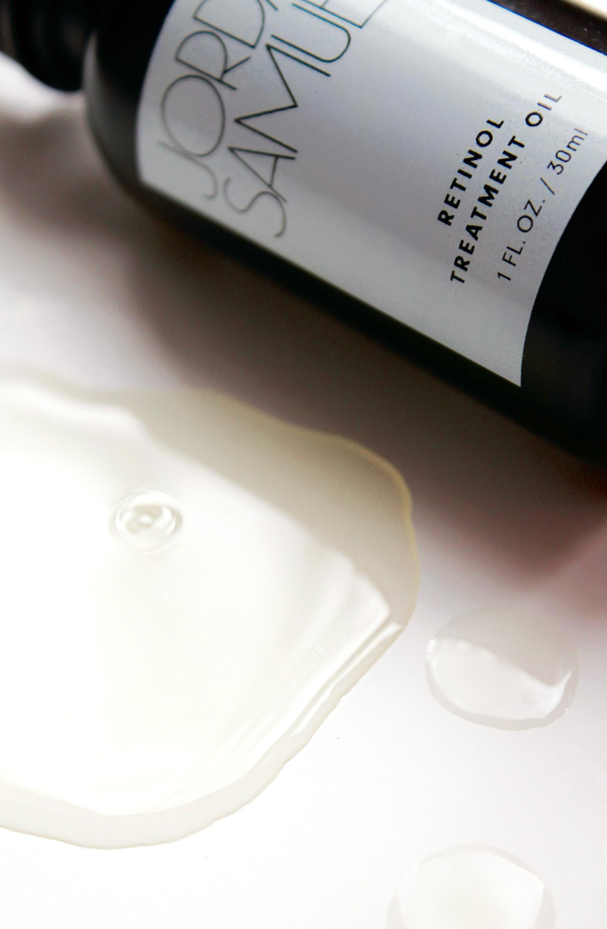 Closely cropped image of The Retinol Treatment Oil's black glass bottle with white label next to one large drop and two smaller droplets of the oil.