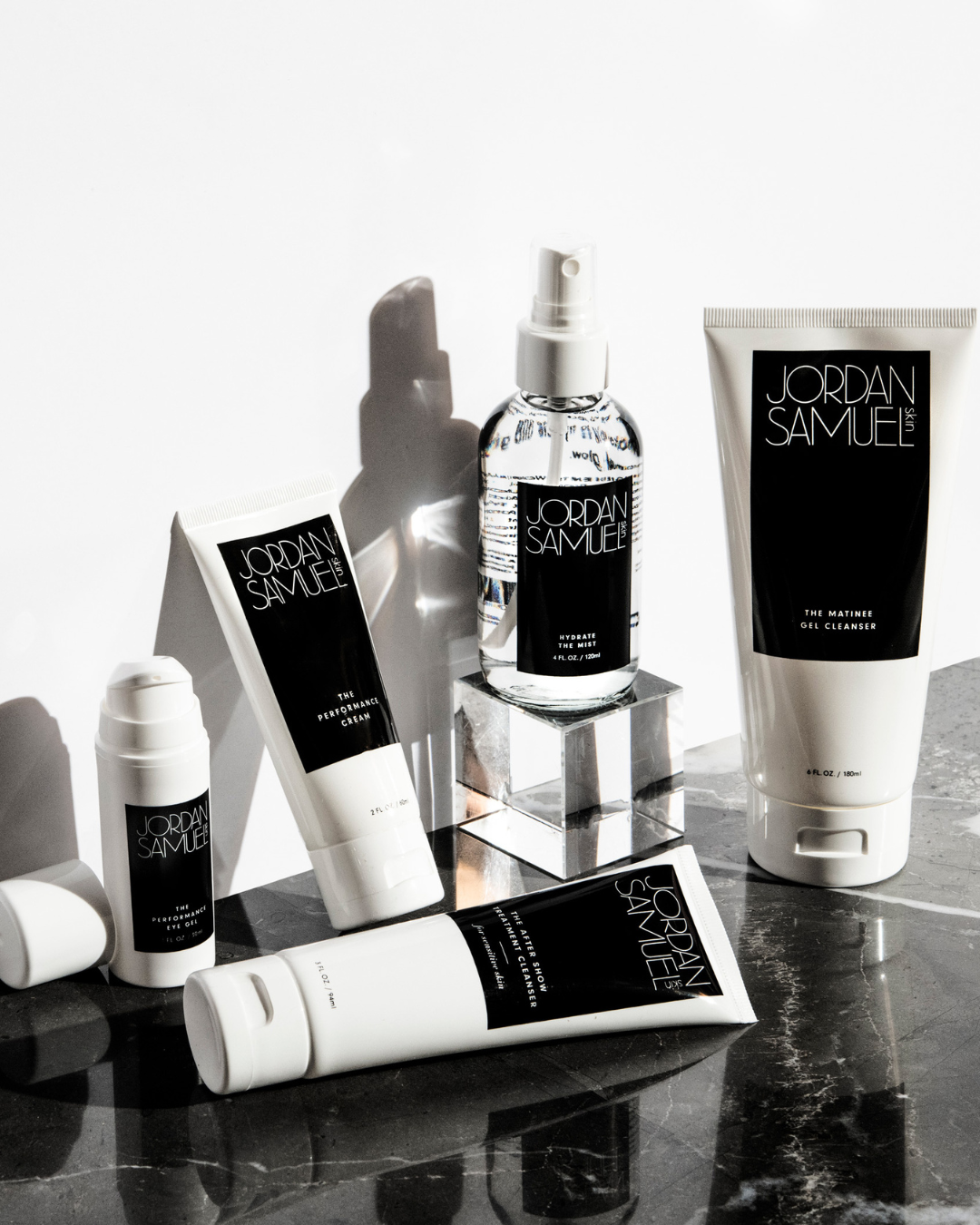 4 brightly-lit JSS products are arranged on a black marble surface up against a stark white wall.